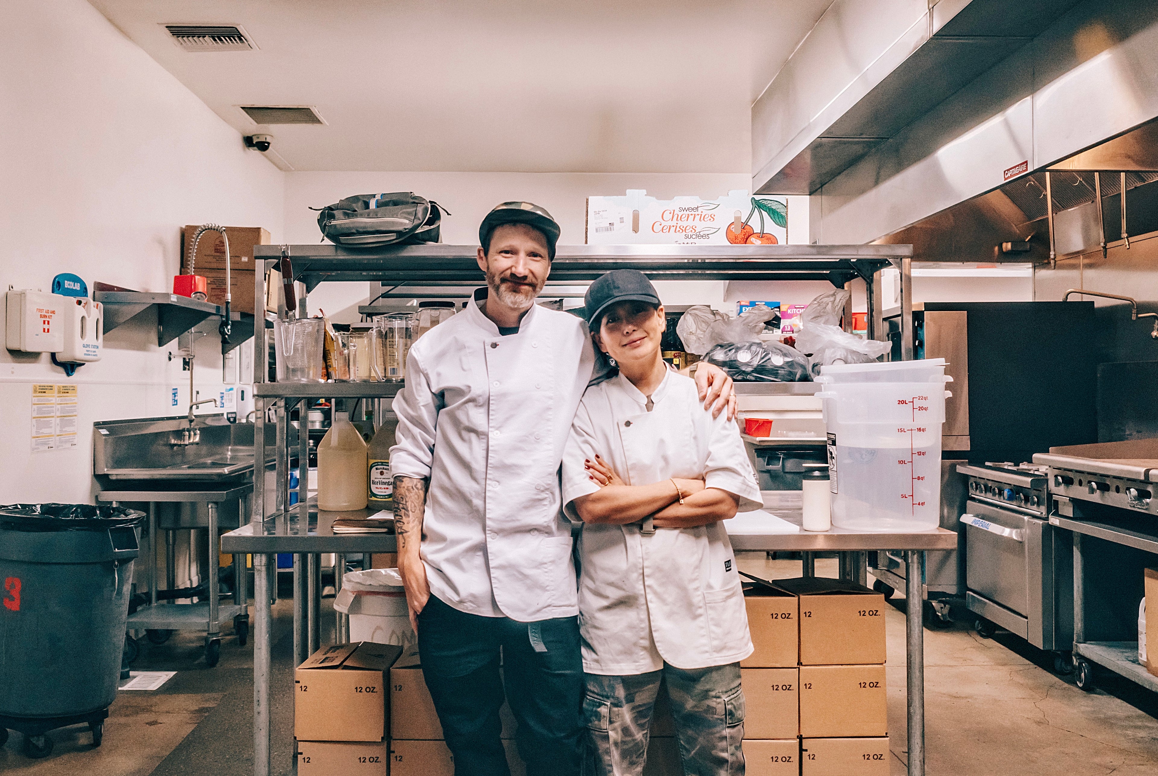 Two chefs posing in a kitchen with various equipment and ingredients around them.